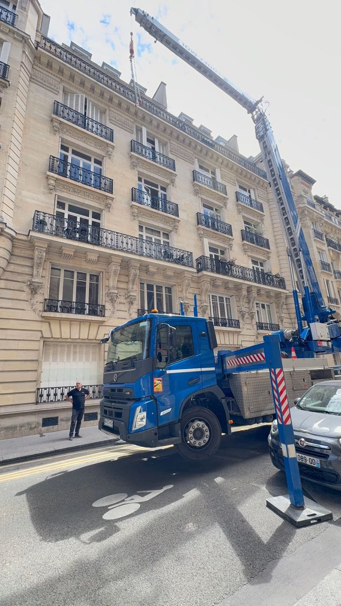 Grue sur camion AÉRO LEVAGE déployée verticalement le long d'une façade haussmannienne du 16e arrondissement de Paris, flèche dépassant le faîtage