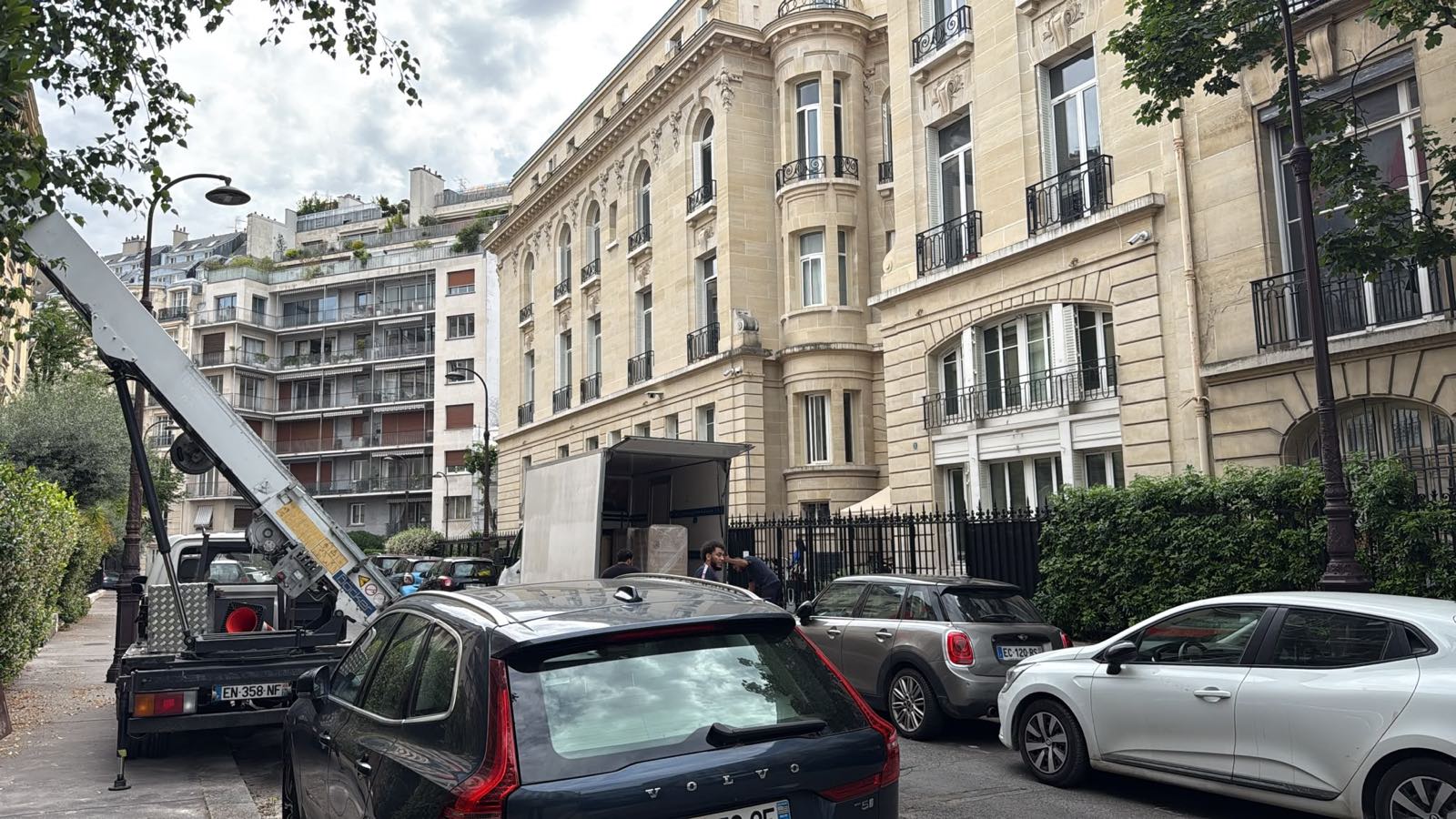 Monte-meuble replié sur son porteur et camion de déménagement ouvert devant un immeuble haussmannien d'angle, Paris 16e