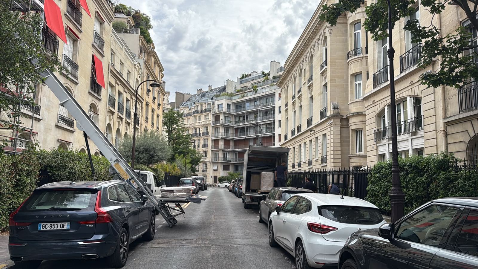 Rue en pente du 16e arrondissement de Paris, monte-meuble déployé le long de la façade et camion de déménagement stationné en aval